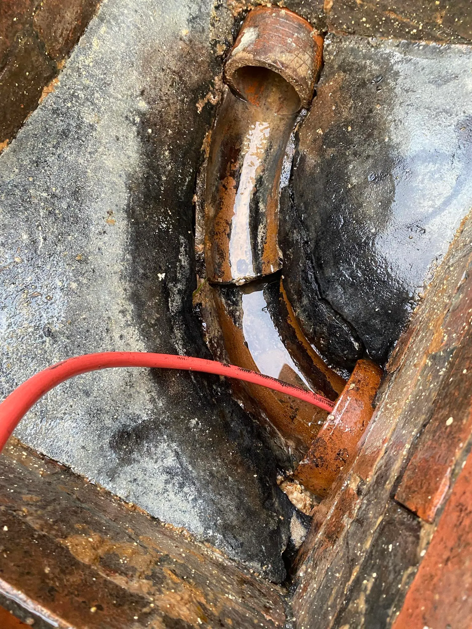 High-pressure water jetting hose being used to clear a blocked drain inside a manhole chamber.