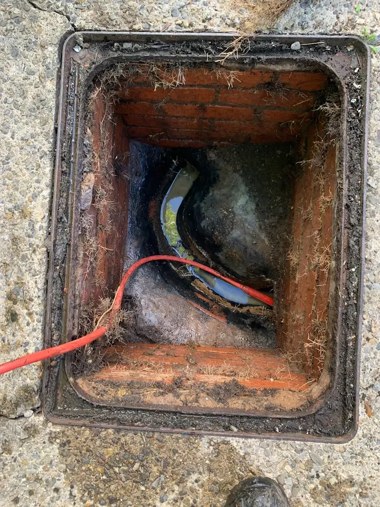 A drain rod is used to clear a blockage in an open inspection chamber.